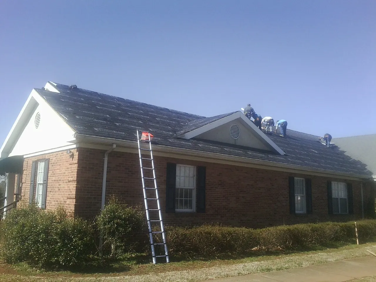 Crew tearing shingles off a brick ranch roof with a ladder set — Emergency Roof Repair work by our crew in Campbell
